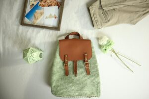 A handcrafted crochet backpack with leather accents alongside travel-themed items in a flat lay composition.