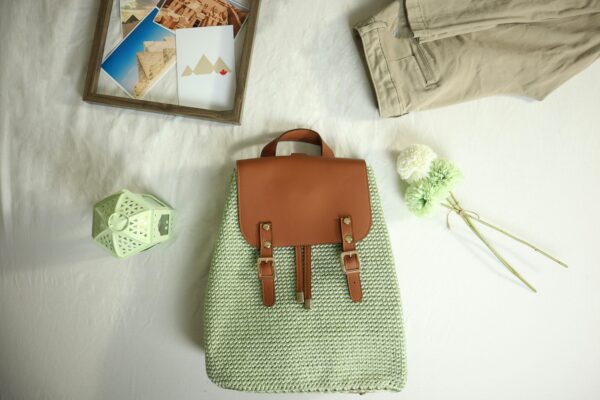 A handcrafted crochet backpack with leather accents alongside travel-themed items in a flat lay composition.