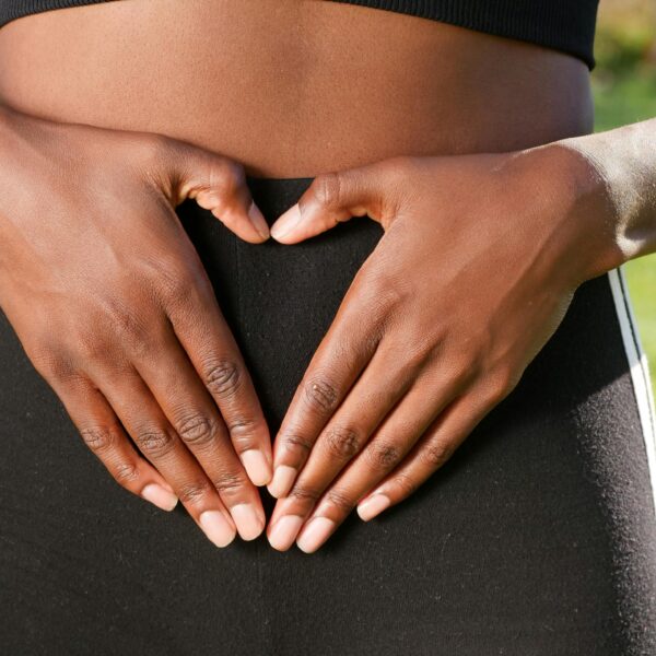 Close-up of hands forming a heart shape on woman's belly, symbolizing health and love.