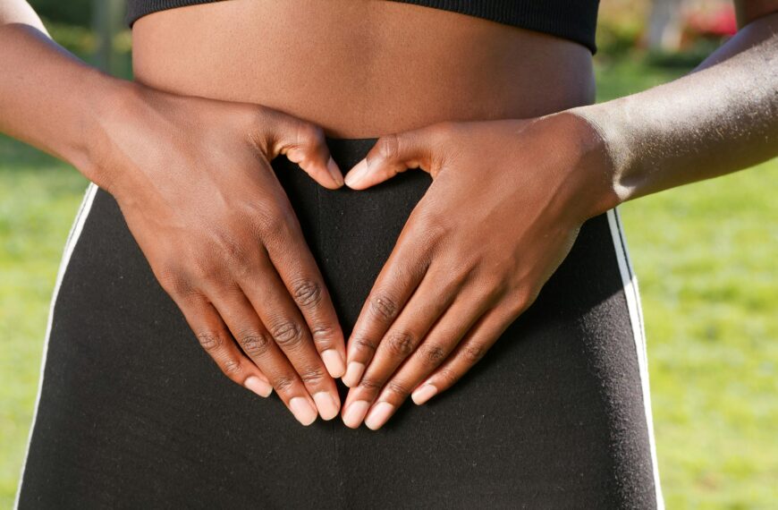 Close-up of hands forming a heart shape on woman's belly, symbolizing health and love.